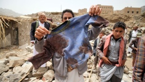 A man displays the bloodied shirt of a child victim at the rubble of houses destroyed by an Saudi air strike in the Okash village near Yemen's capital Source Telesurtv